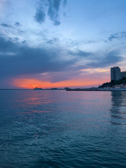 Free Tranquil sunset over the waterfront with buildings and calm sea, capturing a peaceful evening vibe. Stock Photo