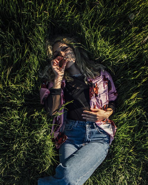 Free A Woman Lying on Green Grass while Smoking Cigarette Stock Photo