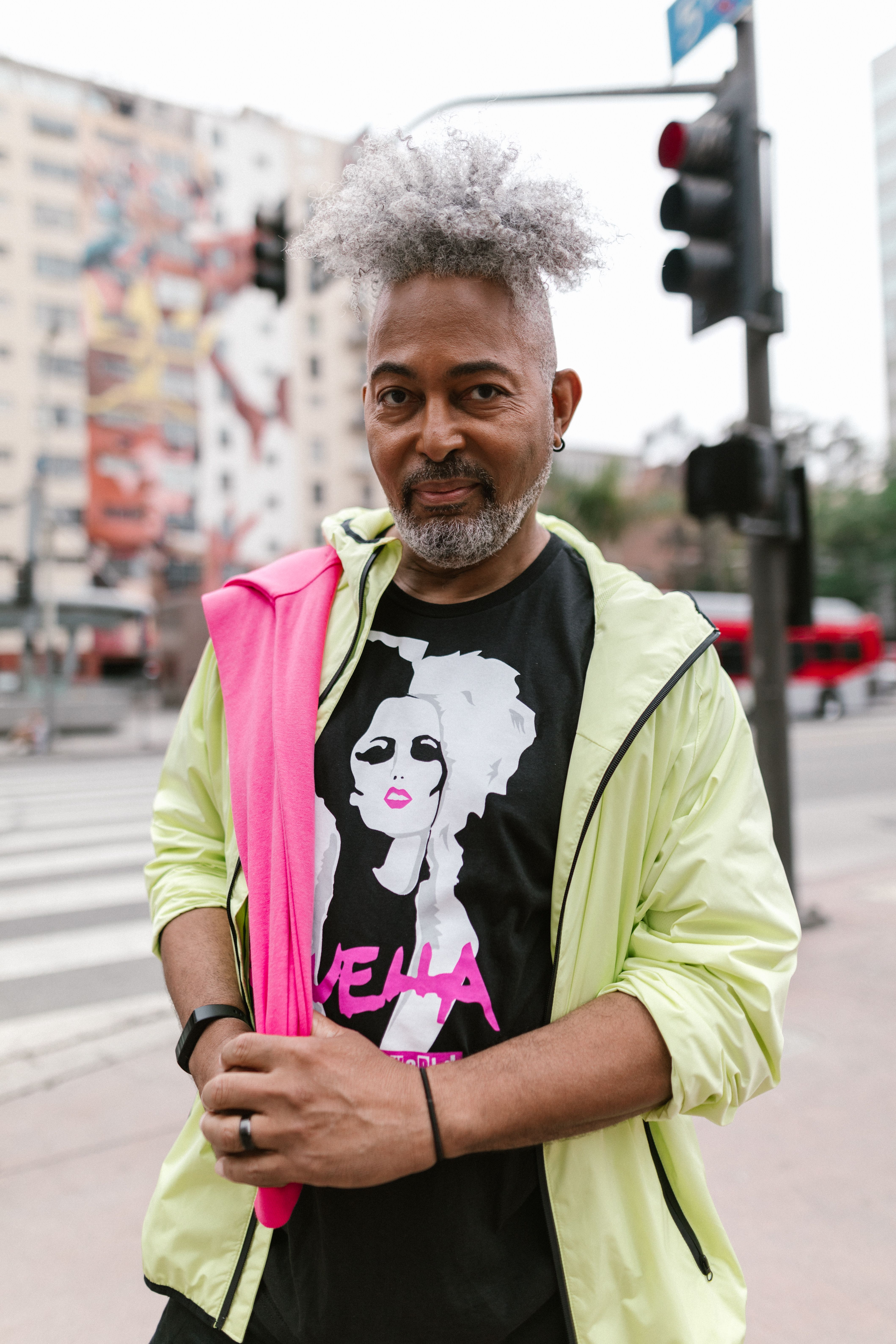 An elegant senior man with afro hair stands confidently in a vibrant streetwear outfit, exuding urban style.