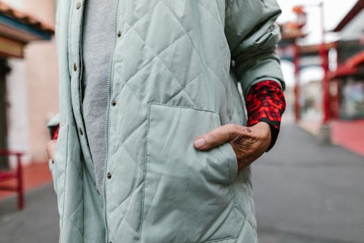 Close-up of an elderly person's hand in pocket wearing a coat on an urban street.