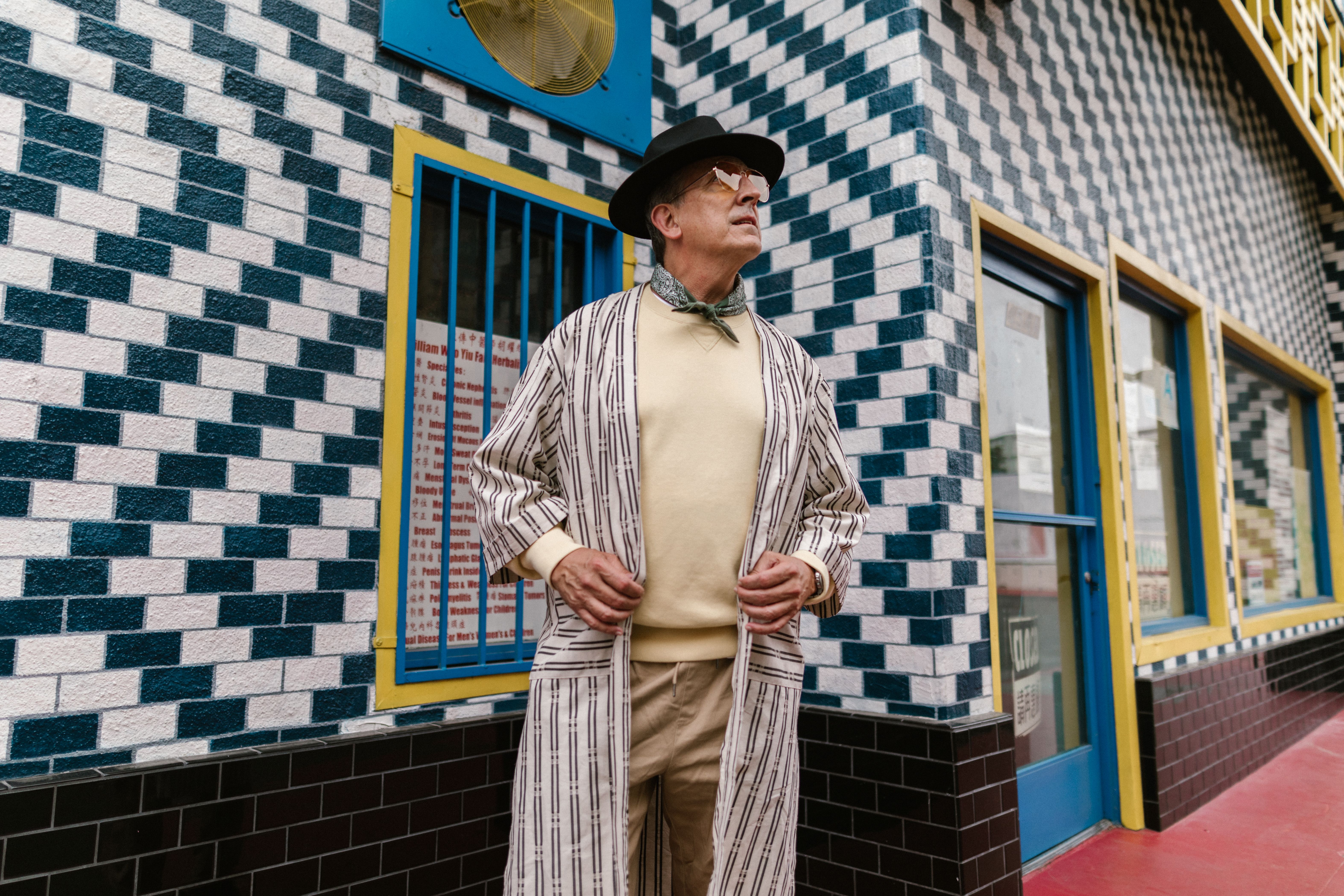 Elderly man in fashionable attire posing on a vibrant geometric patterned street.