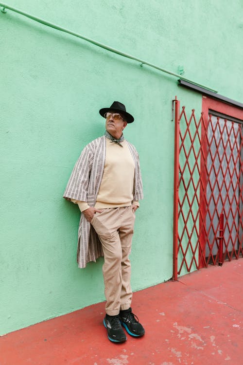 Free Man in Khaki Pants and Black Fedora Hat Standing Beside a Green Wall Stock Photo