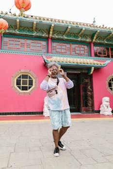 Fashionable man with afro hair and eyeglasses standing in front of a vibrant Asian architectural structure.