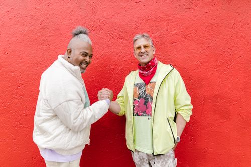 Free Two senior men laughing and posing in casual outfits against a vibrant red wall. Stock Photo