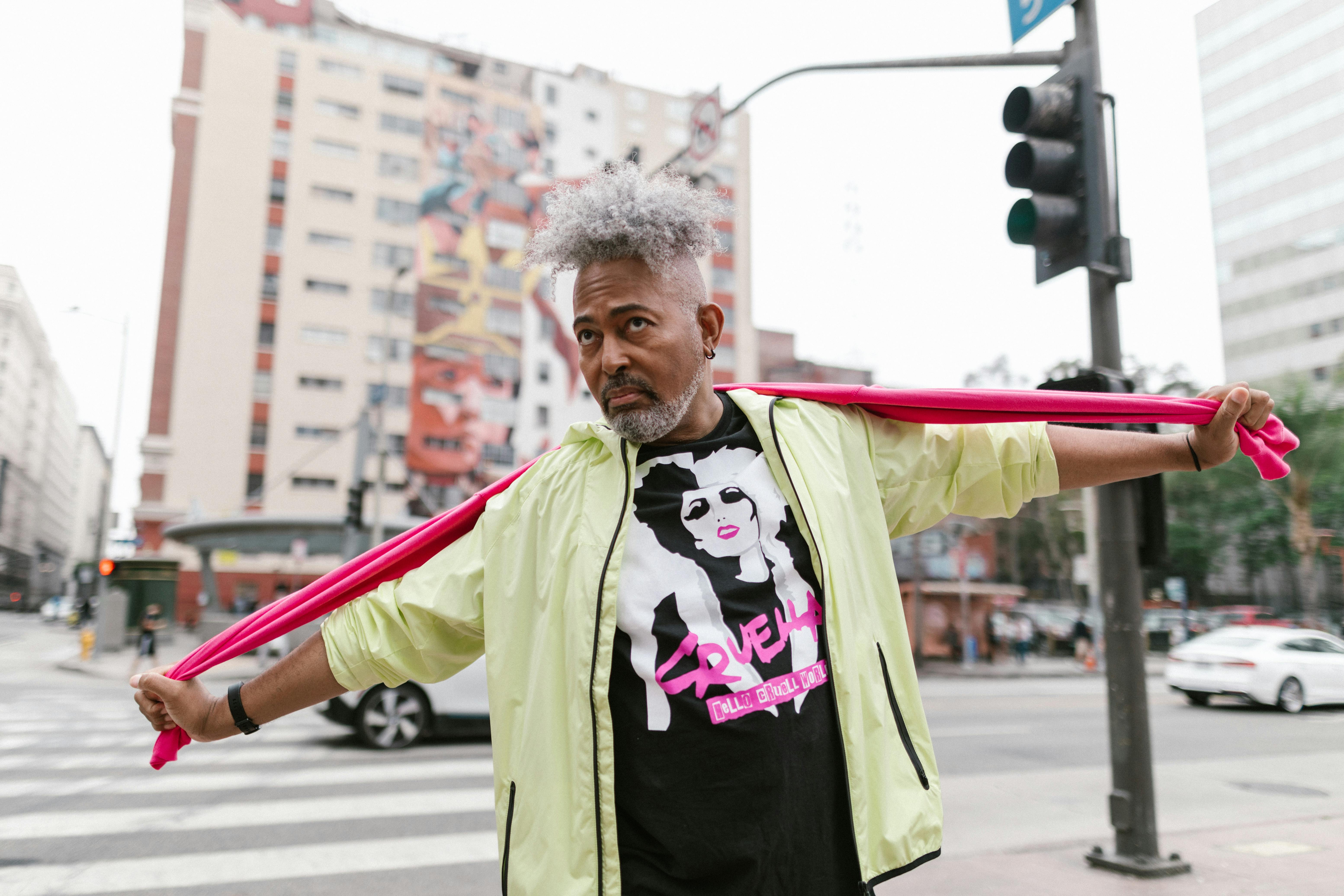 Stylish man in urban environment with a vibrant pink scarf and graphic t-shirt, showcasing modern street fashion.