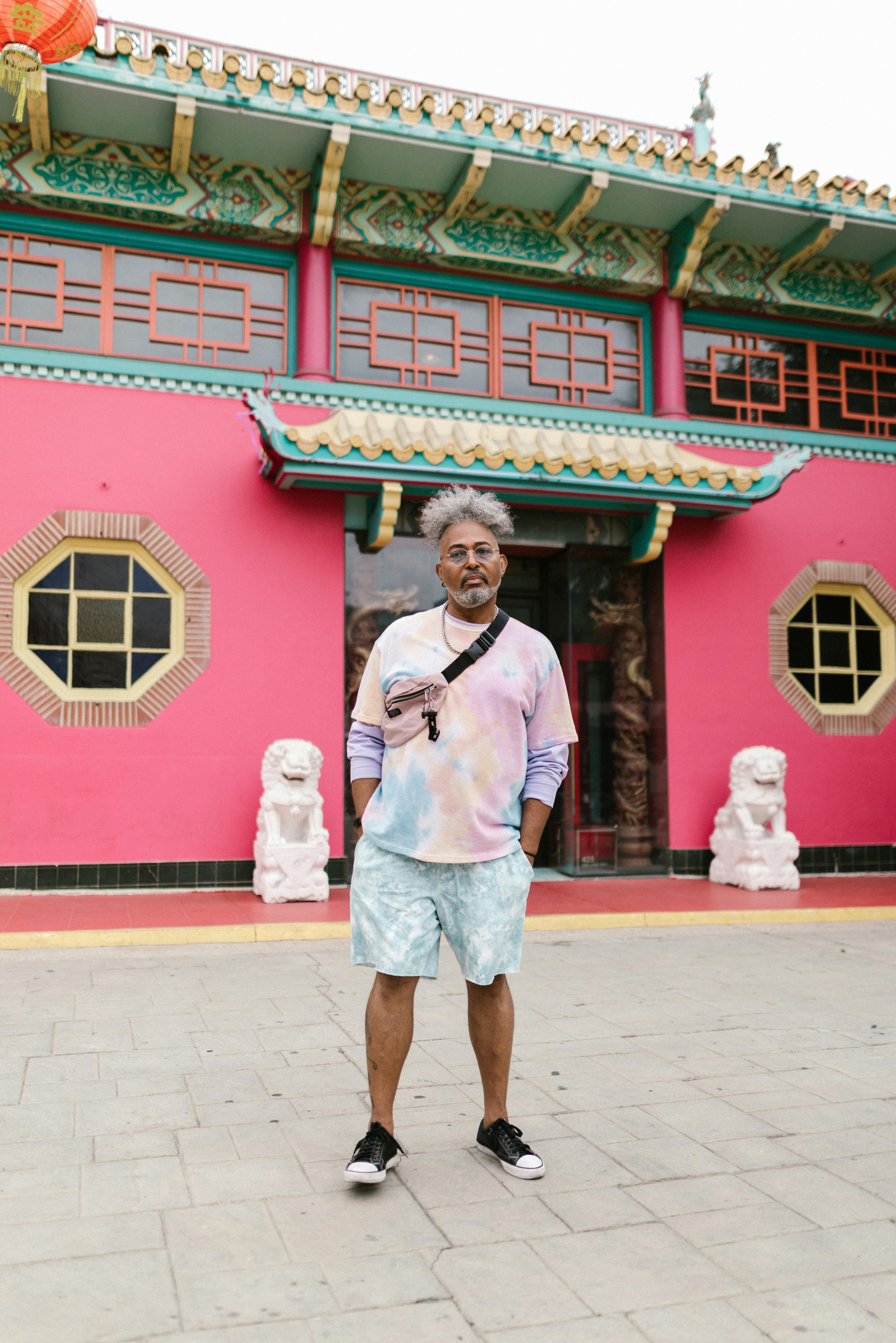 Fashionable man in pastel outfit posing confidently in front of vibrant Asian building, exuding street style.