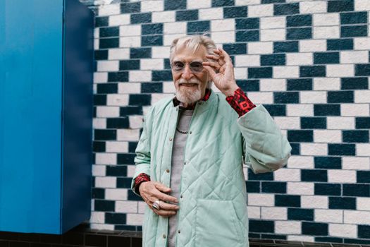 Stylish senior man posing in fashionable streetwear against a brick wall.