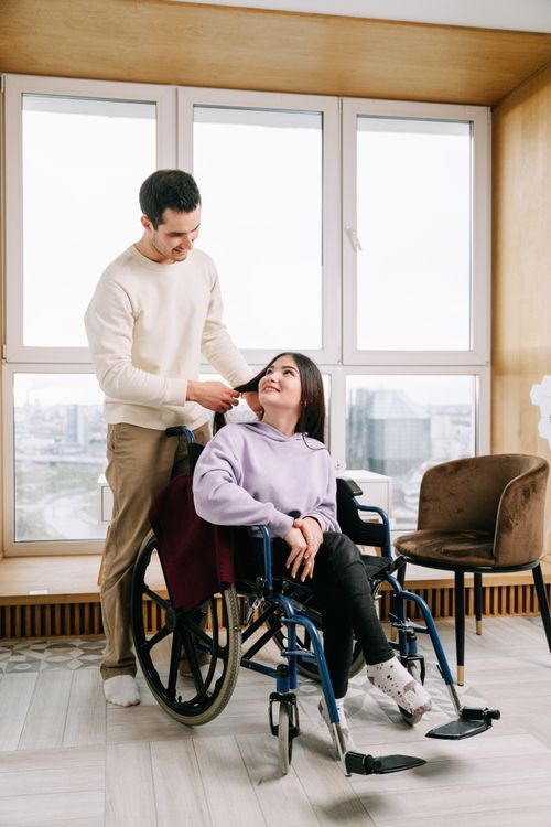 Free A loving couple shares a moment, one sitting in a wheelchair, in a sunlit room. Stock Photo