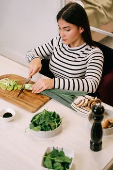 Woman chopping leeks on a wooden board in a modern kitchen setting, surrounded by fresh vegetables.