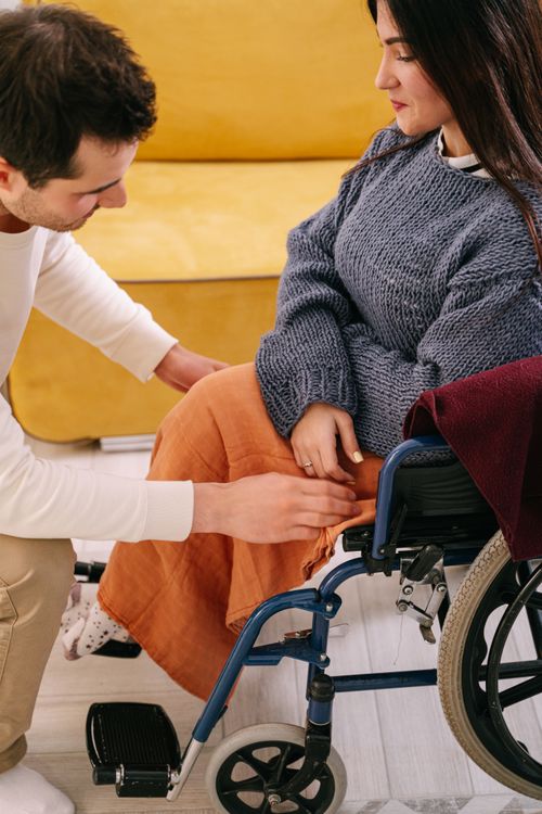 Free A supportive man assisting a woman in a wheelchair indoors, reflecting care and companionship. Stock Photo