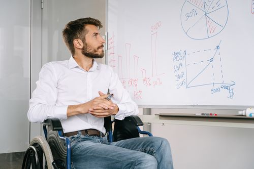 Free Young man in wheelchair analyzing charts on whiteboard in office setting. Stock Photo