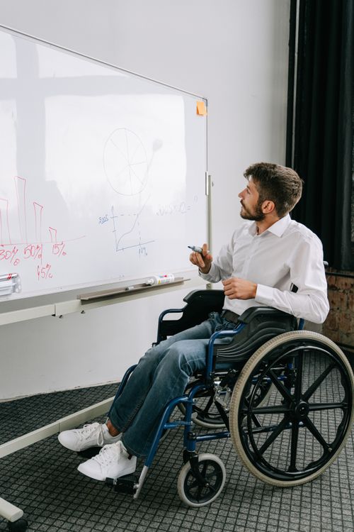 Free A young man in a wheelchair giving a presentation at an office whiteboard. Stock Photo