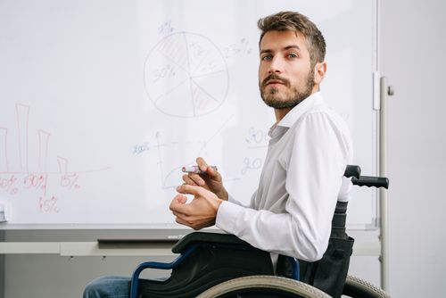 Free Businessman in wheelchair presenting data on whiteboard in office. Diverse and inclusive workplace setting. Stock Photo
