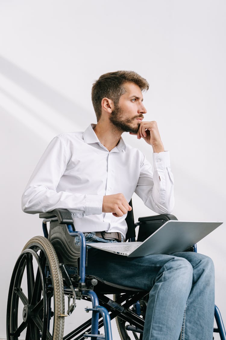 A Man Sitting On A Wheelchair With A Laptop On His Lap