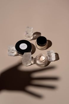 Stylish flat lay of makeup products with dramatic shadows, featuring ice cube props.