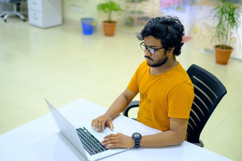 Free A focused South Asian man working on a laptop in a modern office setting. Stock Photo