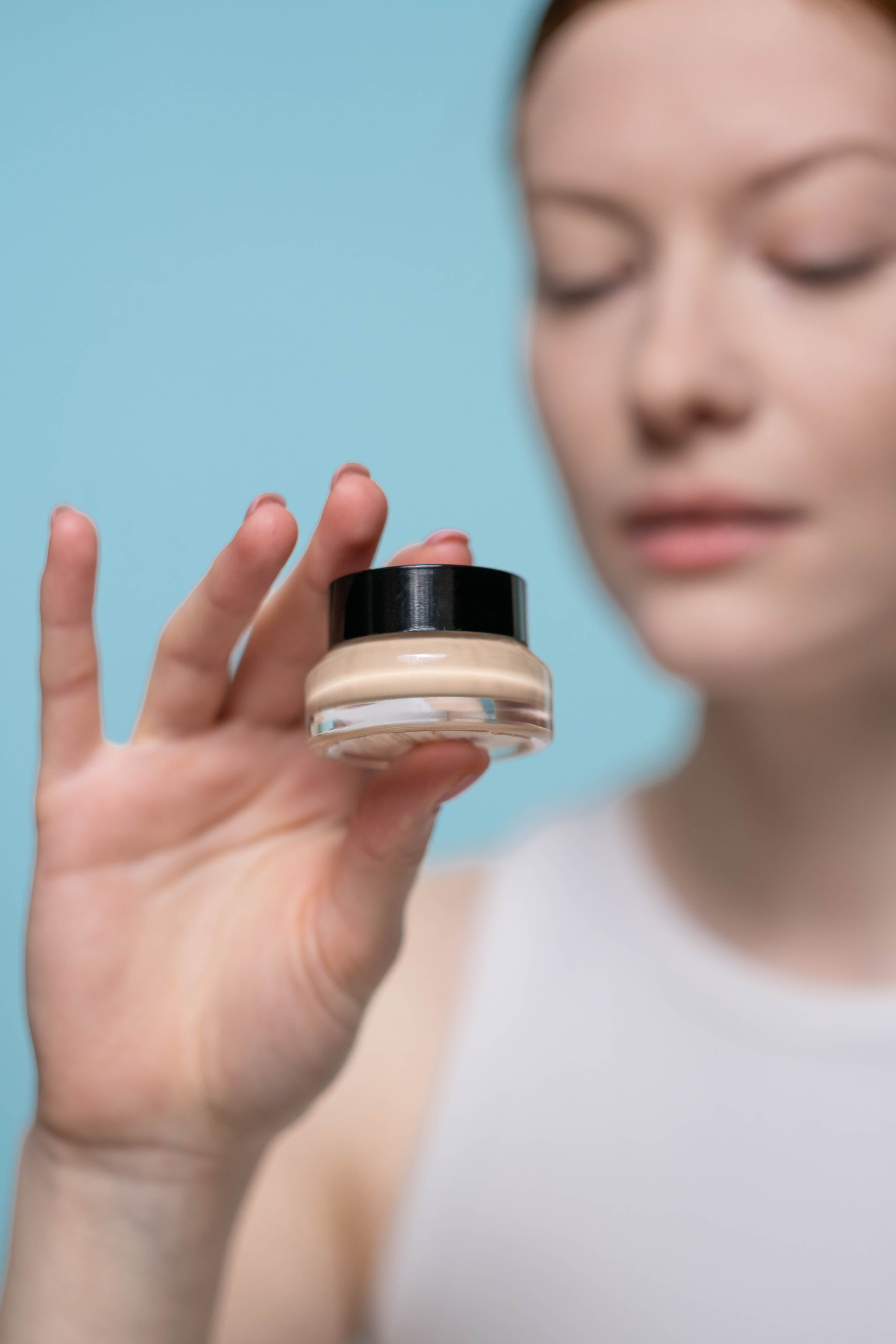 Close-up of a woman holding a skincare cream container against a blue background.