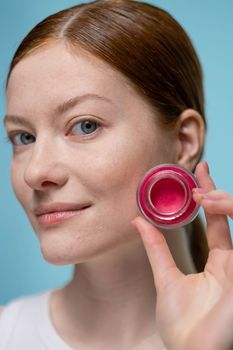 Close-up portrait of a woman showcasing pink cream jar, highlighting beauty and skincare.