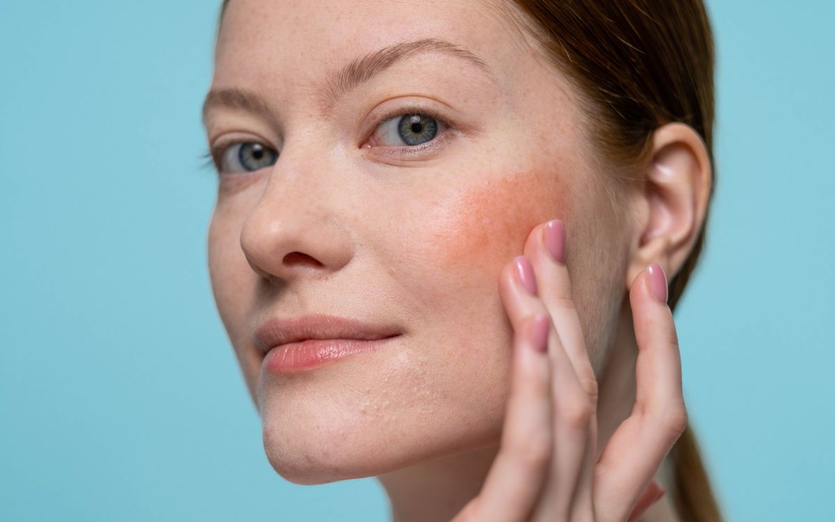 Woman applying blush on her face, highlighting healthy skin and beauty in a studio setting.