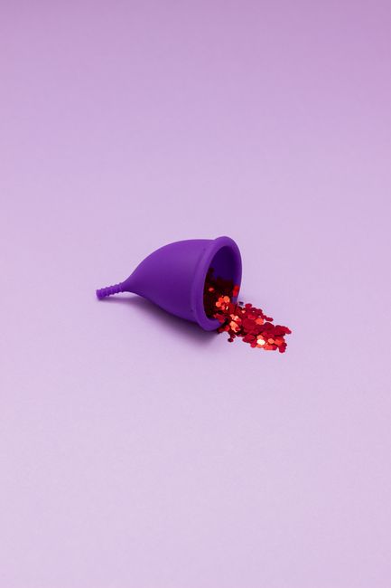 A reusable purple menstrual cup filled with red glitter, set against a lavender background, highlighting eco-friendly feminine hygiene.