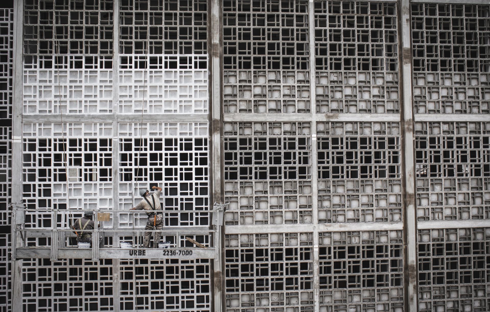 High-rise workers on suspended platform in São Paulo, Brazil, painting geometric facade.