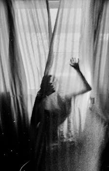 Silhouette of a person behind sheer curtains creates an eerie mood.