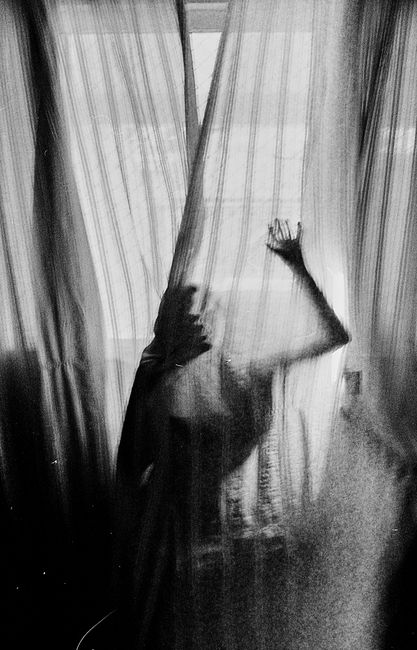 Silhouette of a person behind sheer curtains creates an eerie mood.