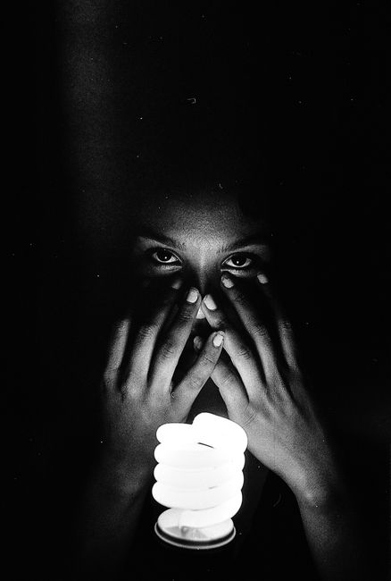Dramatic black and white portrait with a focus on hands covering a face, illuminated by a light bulb.