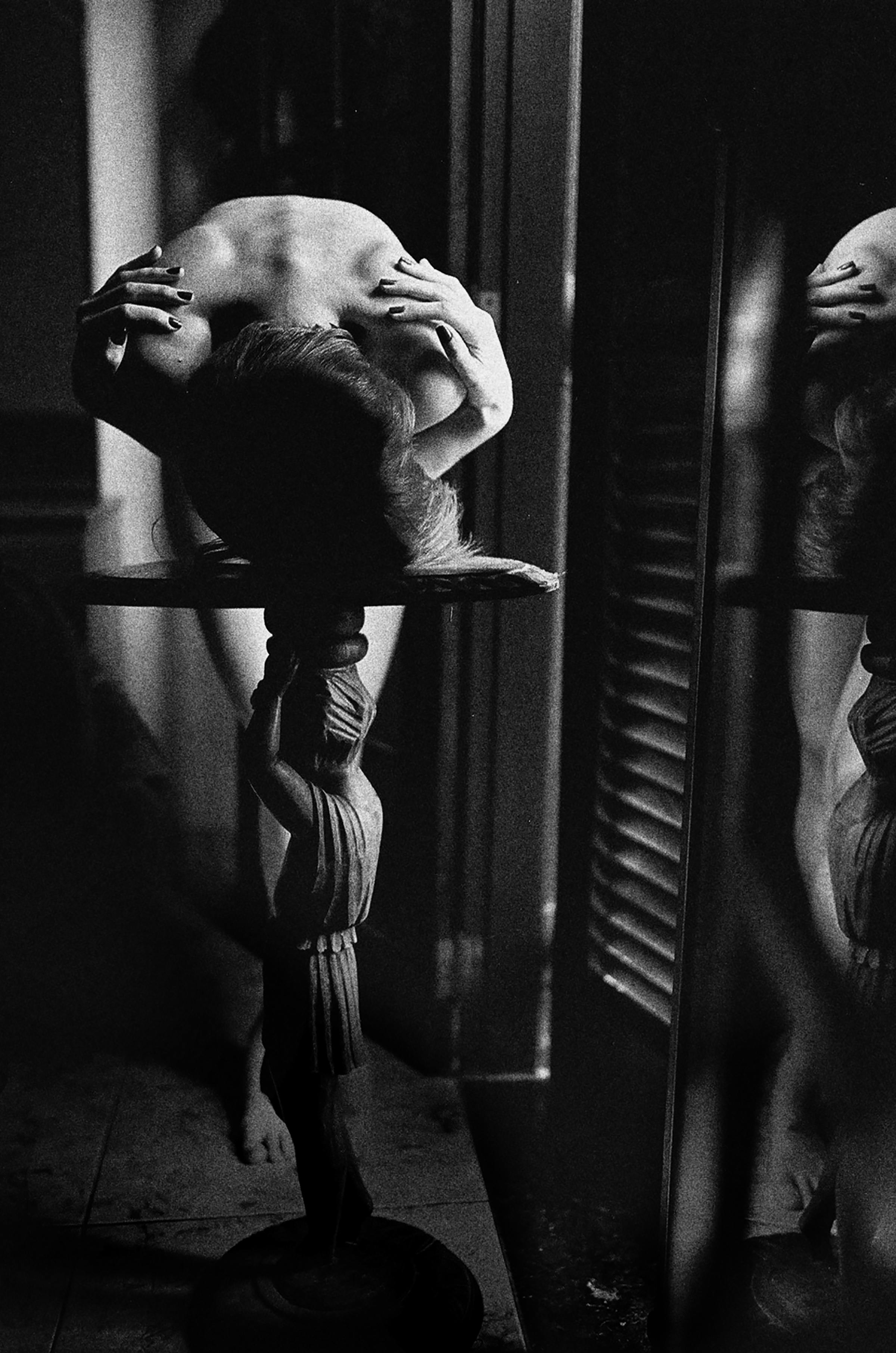 Moody black and white photo of a nude woman in an artistic pose indoors.