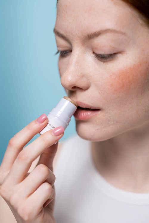 Free Woman using lip balm during beauty routine in studio setting. Stock Photo