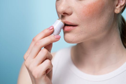 A woman applying lip balm to her lips, highlighting skincare and self-care routine.