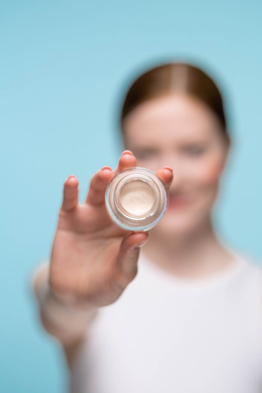 Close-up of a woman showcasing a cosmetic cream jar with a soft focus, highlighting beauty and skincare.