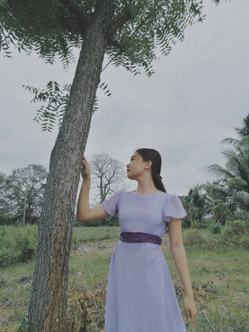 Woman in Purple Dress Standing Beside the Tree