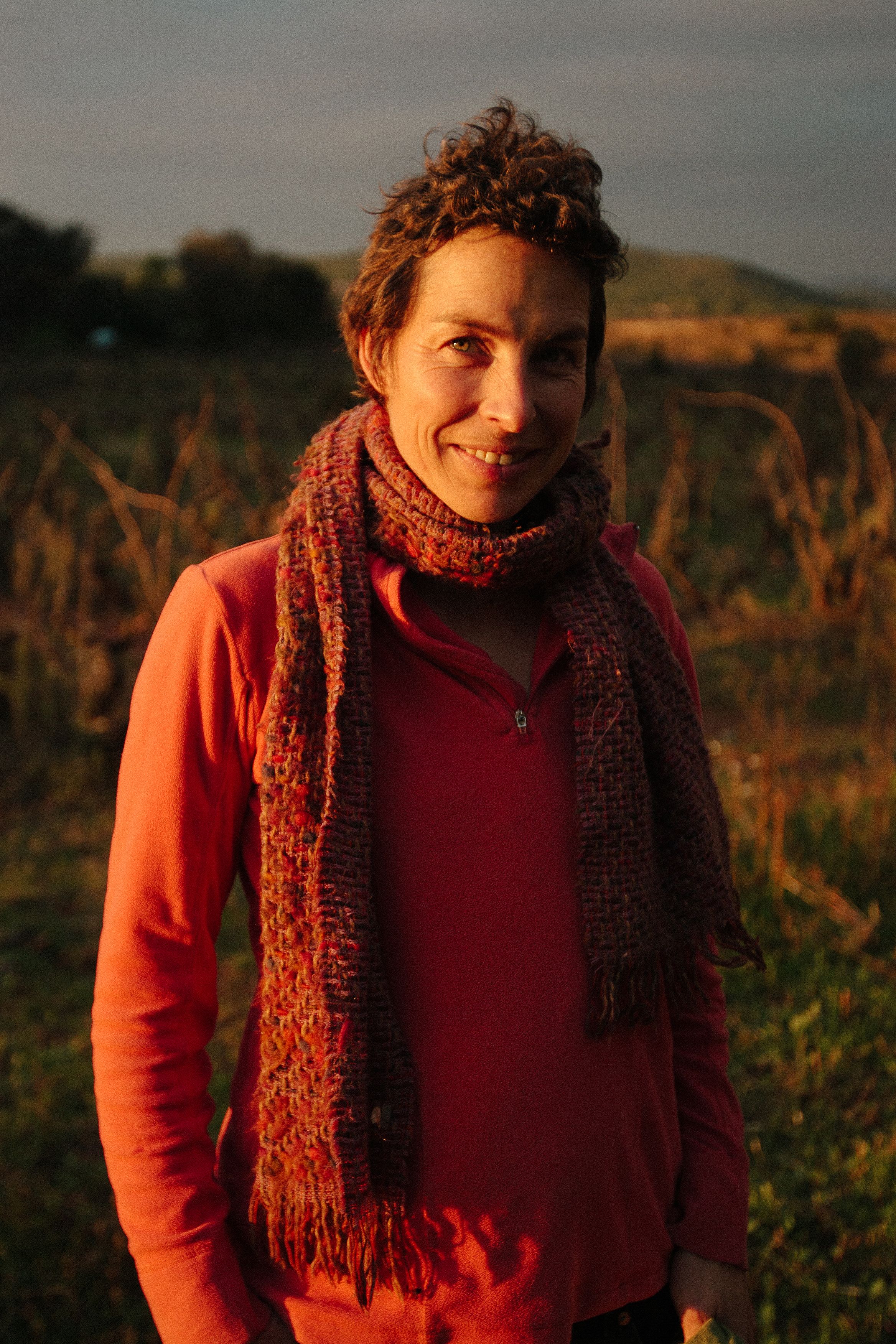 Woman smiling in a warm scarf outdoors, captured during sunset.