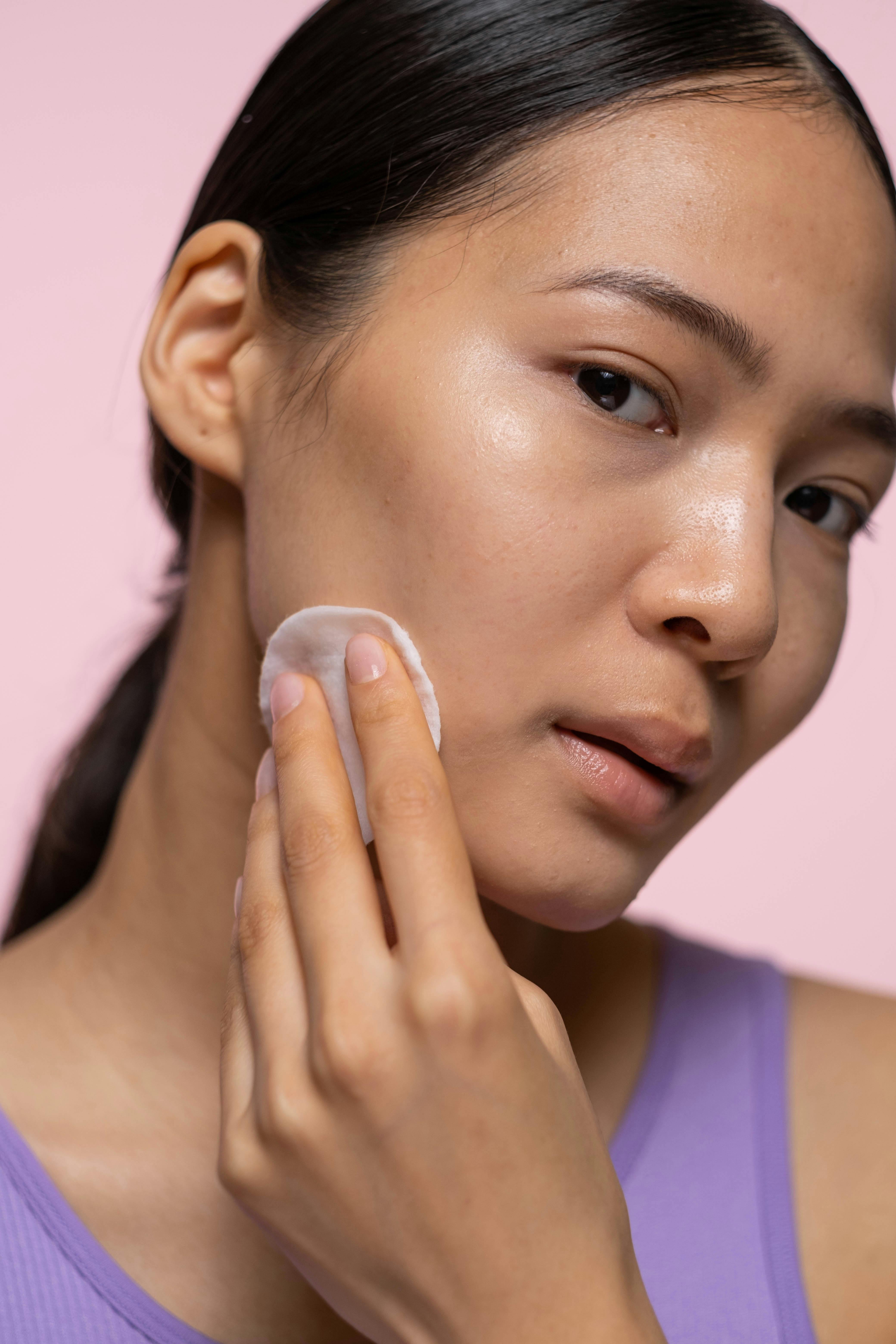 woman in purple tank top applying facial tonic