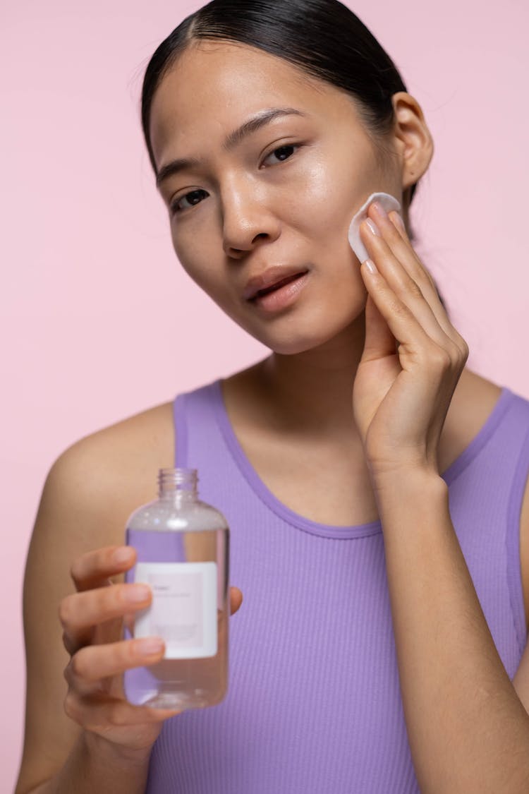 Woman In Purple Tank Top Applying Tonic On Her Face