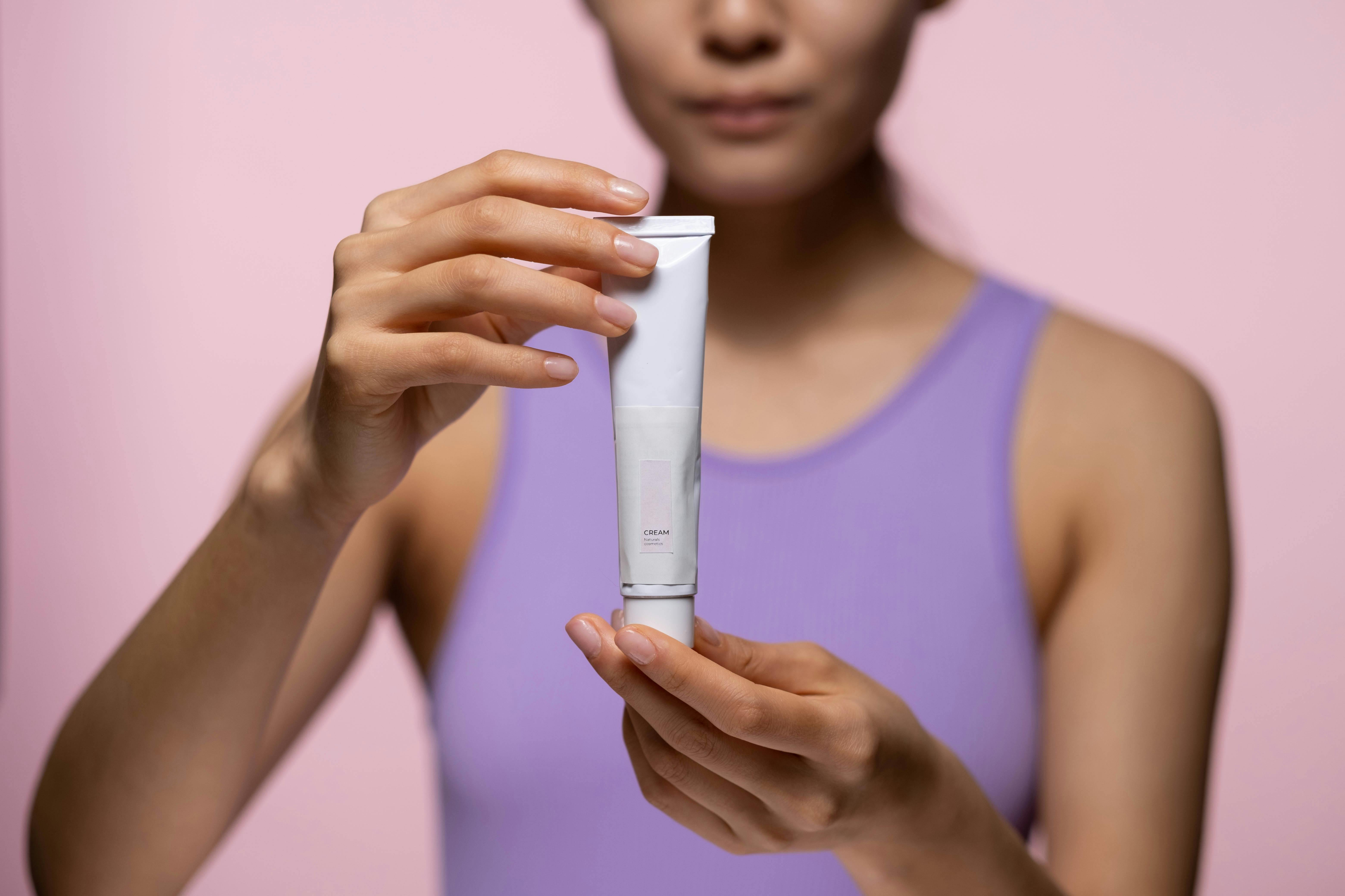 woman in purple tank top holding a cream for hands