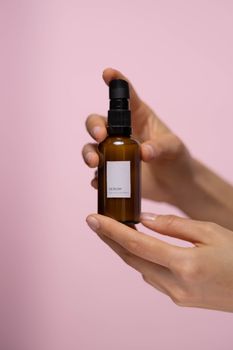 Close-up of hands holding a skincare serum bottle against a pink background, ideal for beauty promotion.