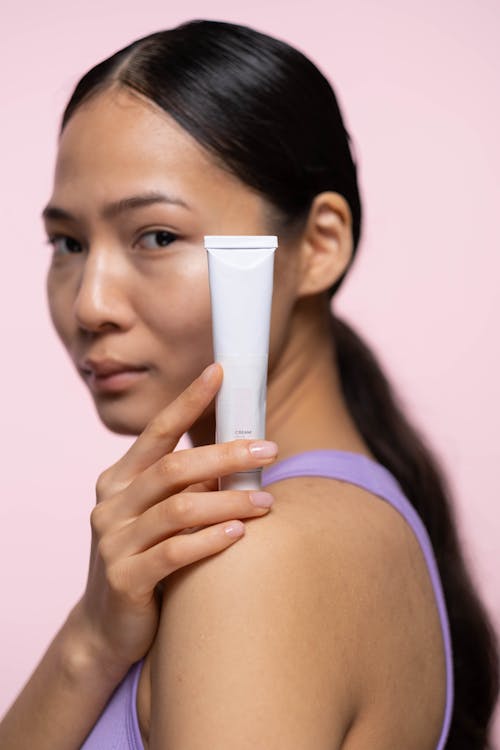 Woman in Purple Tank Top Holding A Cream In White Plastic Tube