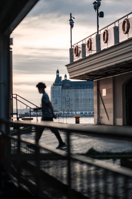 Silhouette of a person walking by waterfront with historic building in background.