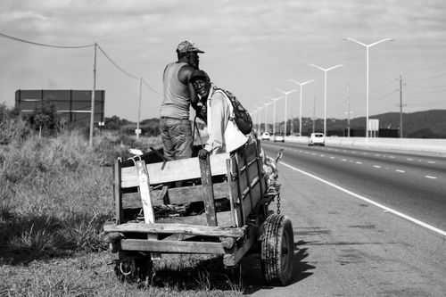 Free Two men on a donkey-drawn cart beside a highway, black and white photo. Stock Photo