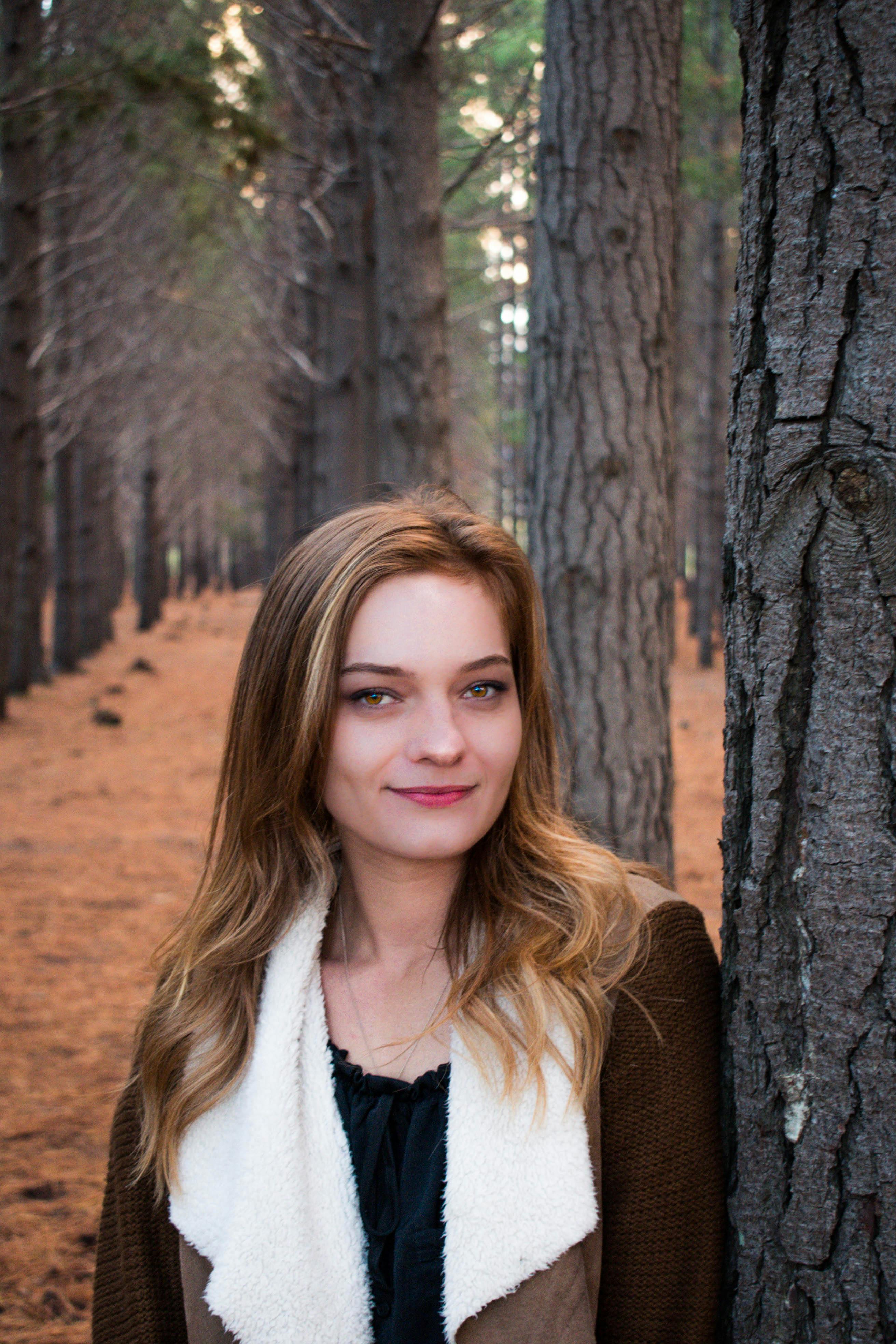 A woman leans against a tree in a serene forest setting during autumn.