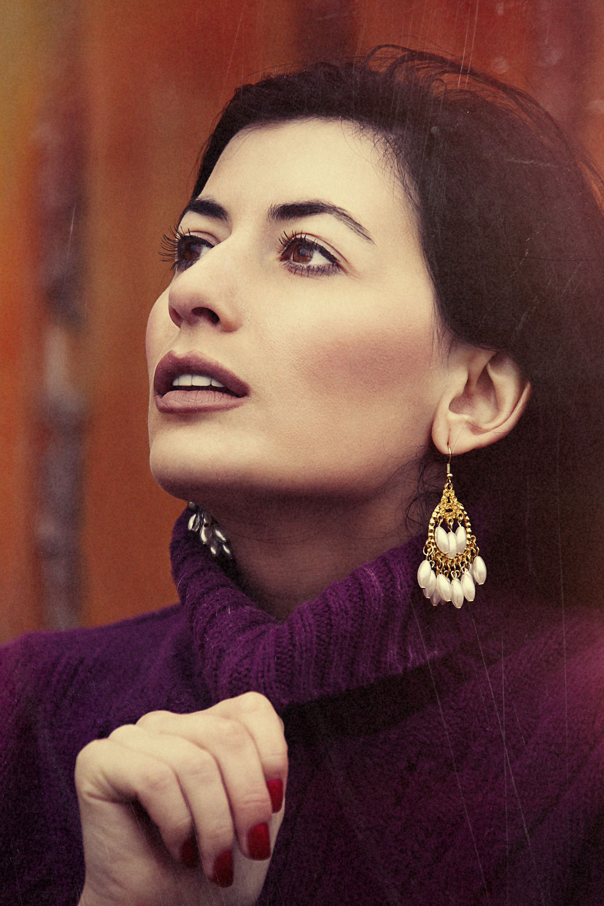 Elegant portrait of a woman in a purple turtleneck sweater with statement earrings.