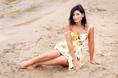 Woman in Floral Dress Sitting on Sand at the Beach