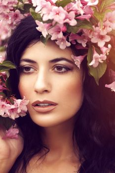 Close-up portrait of a woman with cascading dark hair adorned with pink flowers, creating a serene, natural look.