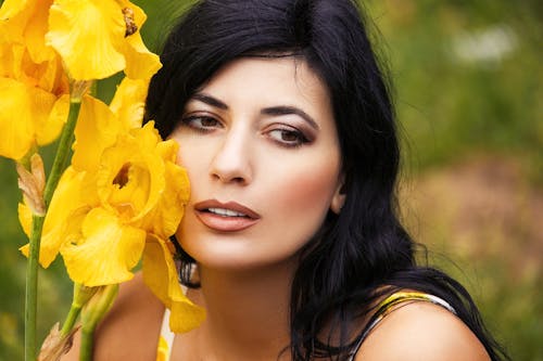 Woman in Yellow and White Spaghetti Strap Top Holding Yellow Flowers