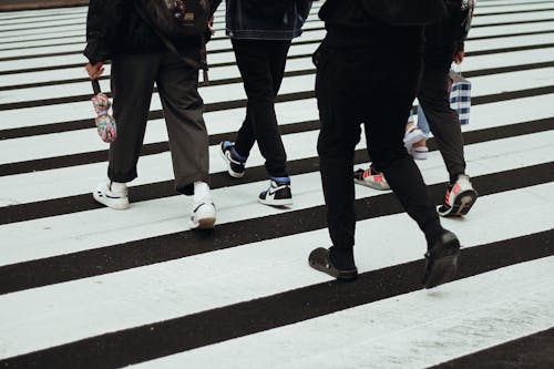 Crop unrecognizable people in casual clothes walking on wide asphalt road with pedestrian crossing in city in daytime