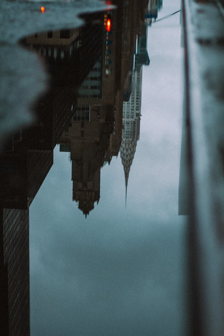 Reflection Of Buildings On Puddle Of Water On Concrete Pavement