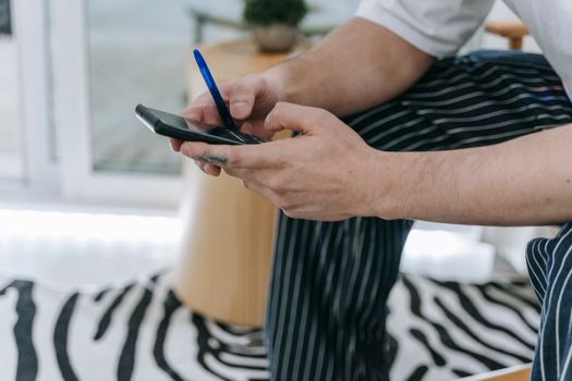 Man in striped pants texting on a smartphone with a blurry background inside a modern room.