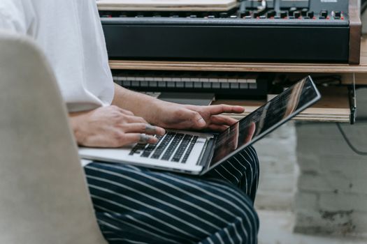 Person typing on laptop near a digital piano, highlighting a tech-savvy music workspace.